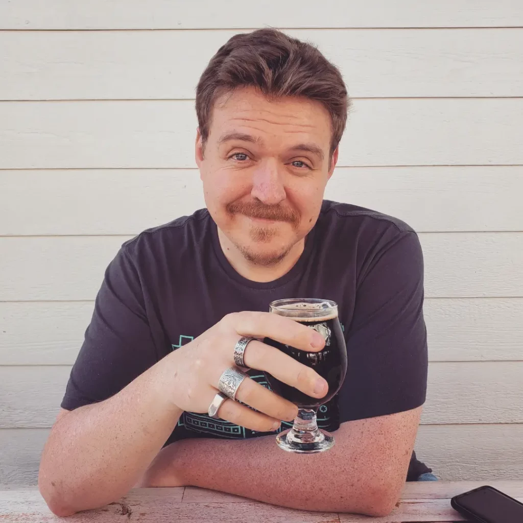 A picture of author Matthew Lyons holding a dark beer.